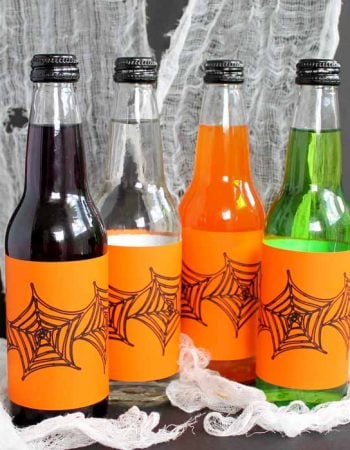 different colors of glass drinks with orange Halloween labels on spider web backdrop